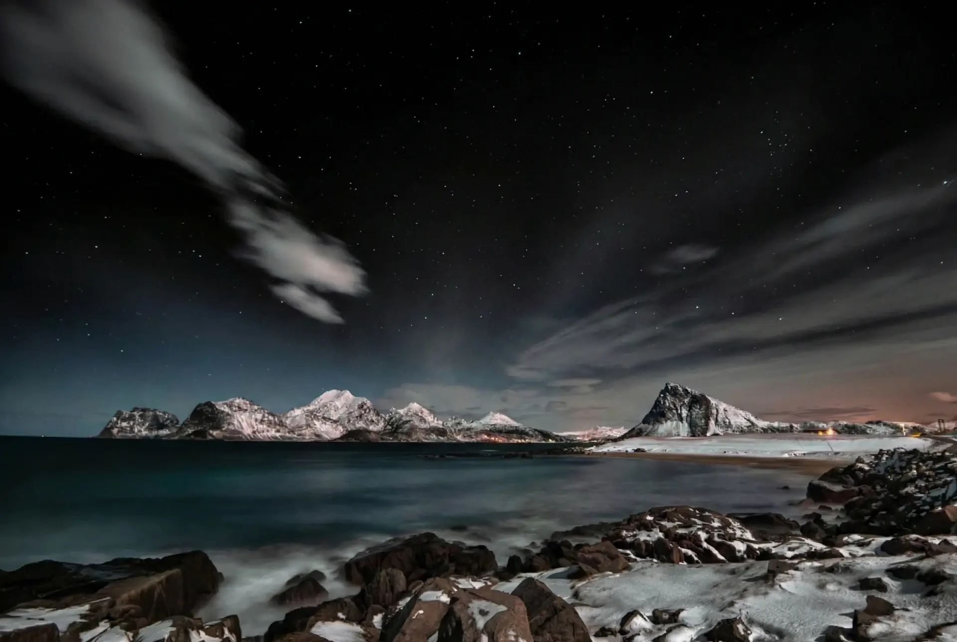 Céu noturno estrelado sobre montanhas nevadas e um lago